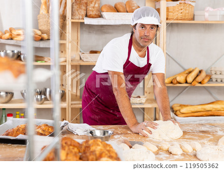 Caucasian guy works in bakery as baker, kneads dough, works with flour. 119505362