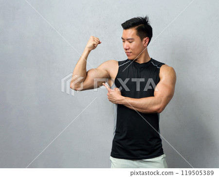 Empowered and strong, a fitness enthusiast male flex his bicep under the stark, vibrant light of a bustling gym, revealing the result of his perseverance and dedication. 119505389