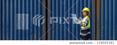Young caucasian woman with safety vest and yellow hardhat checking shipping schedule on clipboard, planning for next shipment. A large cargo container is in the background Young caucasian woman with safety vest and yellow hardhat checking shipping schedule on clipboard, planning for next shipment. A large cargo container is in the background 119505391