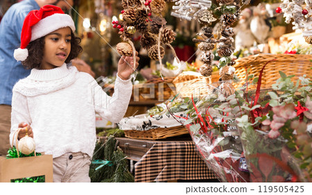 Portrait of joyful small girl in hat choosing Christmas toys 119505425