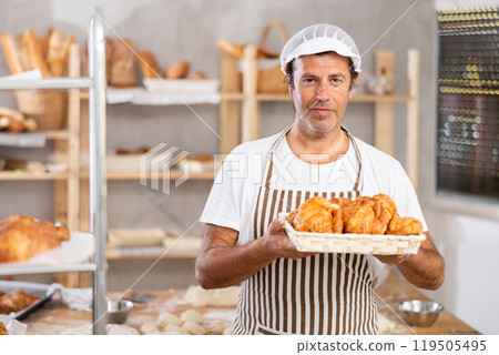 Caucasian male cook-baker worker with basket of croissant, shows many products 119505495