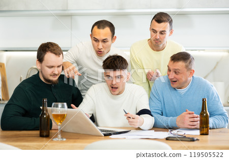 Group of friends watching football match on a laptop together and drinking beer Group of friends watching football match on a laptop together and drinking beer 119505522