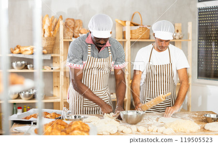 Two male bakers shaping dough pieces and rolling out 119505523