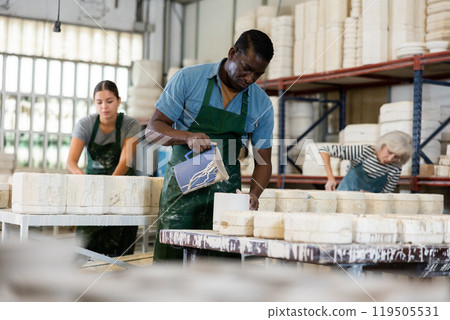 Slip casting - african american worker pours slip mass from jug into plaster mold in pottery factory 119505531