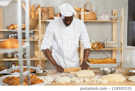 Making yeast dough in bakery - male baker rolling out dough with rolling pin 119505535
