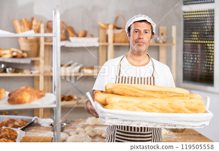 Caucasian male cook-baker worker with basket of baguettes, shows many products 119505558