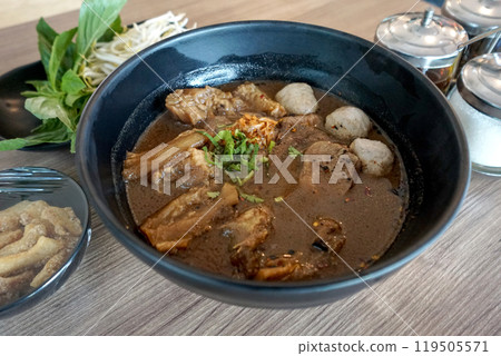 Premium thai style beef boat noodle in dark soy sauce, pickled bean curd, and some other spice soup served with meatball, tendon and braised shank. Bunch of noodle condiment are on the table. Premium thai style beef boat noodle in dark soy sauce, pickled bean curd, and some other spice soup served with meatball, tendon and braised shank. Bunch of noodle condiment are on the table. 119505571