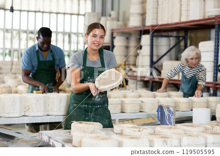 Positive young worker demonstrates half of plaster mold for pottery in pottery factory Positive young worker demonstrates half of plaster mold for pottery in pottery factory 119505595