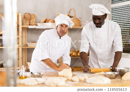 Two bakers working to knead and roll dough in bakery Two bakers working to knead and roll dough in bakery 119505613