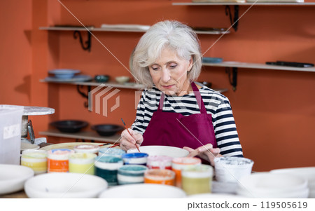 Mature woman ceramist painting new crafted plate Mature woman ceramist painting new crafted plate 119505619