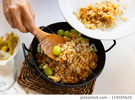 Womens hands with spatula lay out porridge made of bread crumbs, bacon and sausages chorizo - migas 119505620