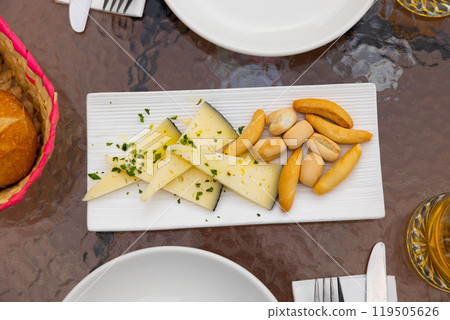 Slices of semi-hard spanish manchego sheep cheese sprinkled with chopped herbs and crutones at plate 119505626