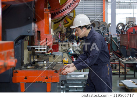 A man in a hardhat and mechanic coverall dust protection suit using a machine to shape metal parts safely. Atmosphere in manufactory with large machinery. 119505717