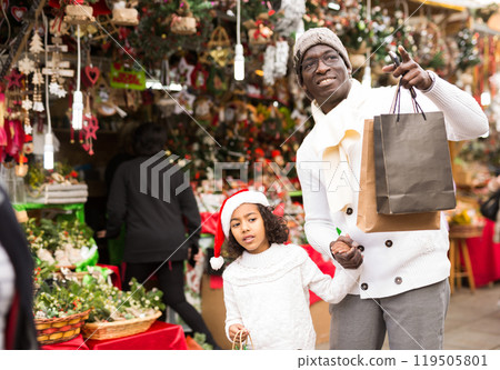 Smiling girl and father with paper bags choosing Christmas toys Smiling girl and father with paper bags choosing Christmas toys 119505801