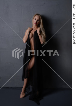 Woman poses confidently in a sheer black robe against a gray wall backdrop Woman poses confidently in a sheer black robe against a gray wall backdrop 119506291