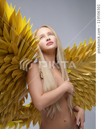 A model poses gracefully with large golden feathered wings in a studio setting 119506301