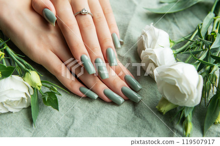 Elegant hands adorned with green nail polish surrounded by white roses and greenery on a soft fabric Elegant hands adorned with green nail polish surrounded by white roses and greenery on a soft fabric 119507917