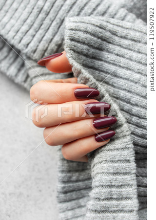 A person holding a gray sweater while showcasing perfectly manicured maroon nails A person holding a gray sweater while showcasing perfectly manicured maroon nails 119507922