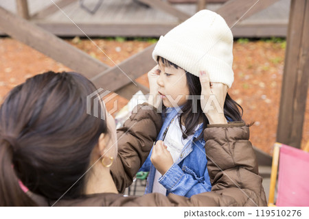 A mother puts a hat on her daughter at a campsite 119510276