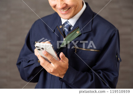 A middle-aged male businessman wearing work clothes laughing while looking at his smartphone 119510939