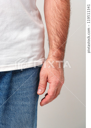 A close-up view of a man's bare hand resting against his side 119511341