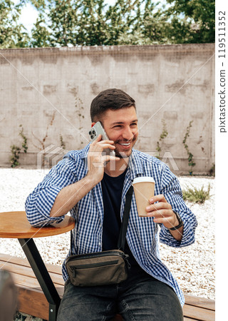 Cheerful man talking on his phone while enjoying coffee at an outdoor cafe 119511352