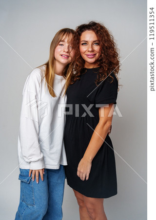 Two women standing together, one in white and the other in black, showcasing a warm connection 119511354