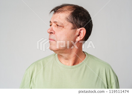 Man in a green shirt gazing thoughtfully to the side in a minimalist setting 119511474