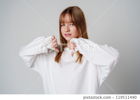 Young teen girl expressing disapproval while wearing a white oversized sweater against a plain backdrop 119511490
