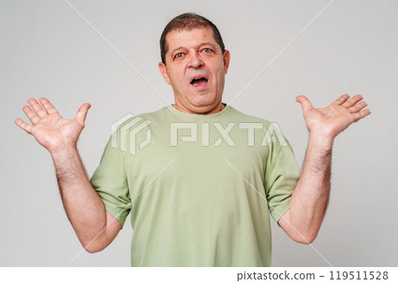 A surprised man in a green shirt expressing astonishment against a light background 119511528