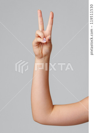 A hand showing the peace sign against a simple gray background 119511530