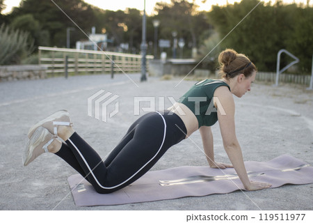 Young woman doing push-ups on a fitness mat outdoors 119511977