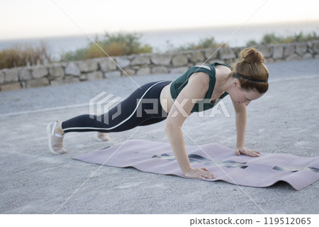 Young woman doing push-ups on fitness mat outdoors 119512065