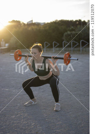 Woman doing squats with weights outdoors 119512070
