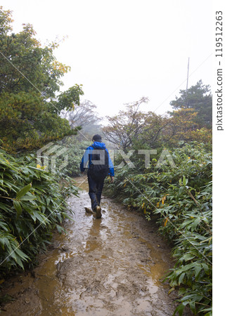A boy climbing a mountain in the rain 119512263