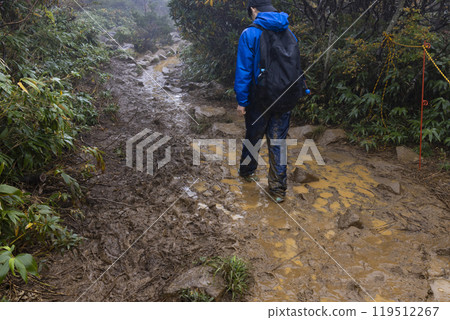 A boy climbing a mountain in the rain 119512267