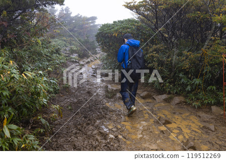 A boy climbing a mountain in the rain 119512269