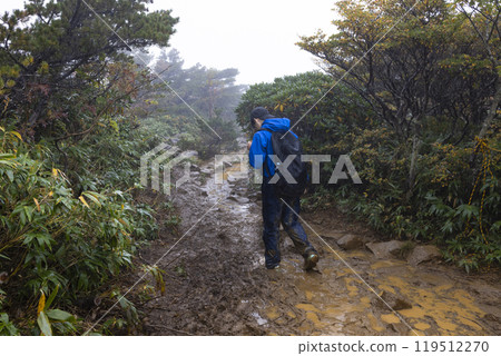 A boy climbing a mountain in the rain 119512270