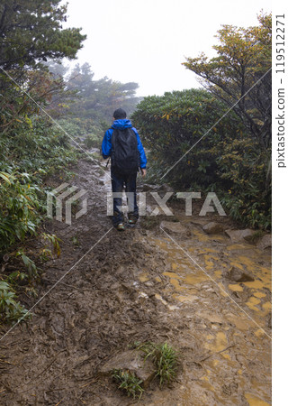 A boy climbing a mountain in the rain 119512271