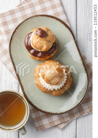Religieuse pastry is composed of two choux buns filled with pastry cream, topped with chocolate ganache and decorated with cream closeup on the plate. Vertical top view 119512453