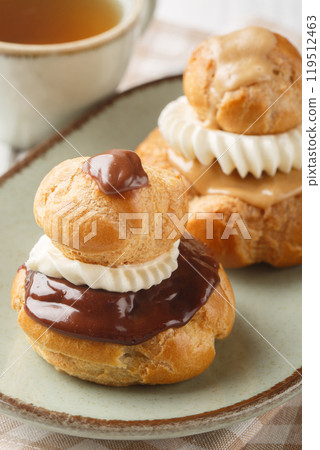 Religieuse French cake made of a small choux pastry stacked on top of a larger one filled with cream patissier, flavoured with chocolate or mocha closeup on the plate. Vertical 119512463