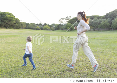 Mother and son running through park on sunny day 119512657