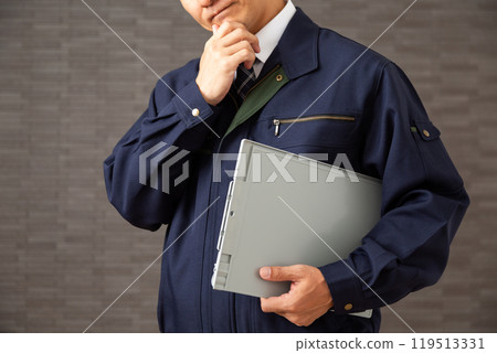 A middle-aged male businessman wearing work clothes holding a binder and worrying A middle-aged male businessman wearing work clothes holding a binder and worrying 119513331