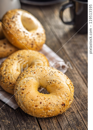 Bagel sprinkled with fried onion, sesame and poppy seeds on wooden table. Bagel sprinkled with fried onion, sesame and poppy seeds on wooden table. 119513595