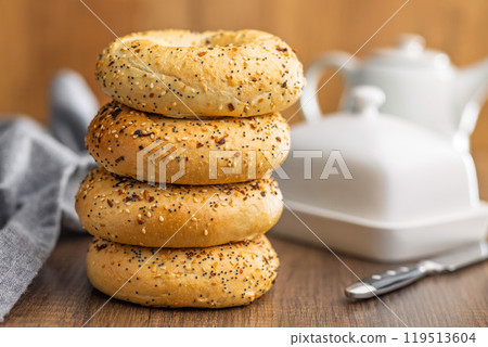 Bagel sprinkled with fried onion, sesame and poppy seeds on wooden table. Bagel sprinkled with fried onion, sesame and poppy seeds on wooden table. 119513604