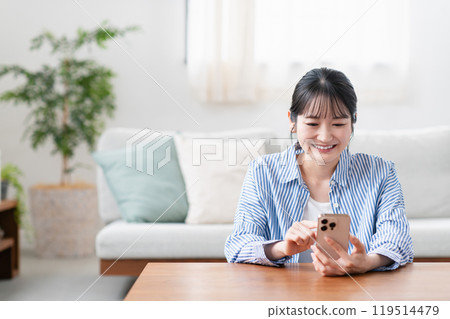 A young woman operating a smartphone in the living room A young woman operating a smartphone in the living room 119514479