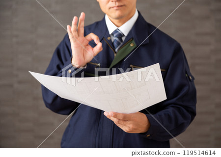 一位穿著工作服的中年商人看著房屋圖紙,在一個圓圈上簽名。 一位穿著工作服的中年商人看著房屋圖紙,在一個圓圈上簽名。 119514614