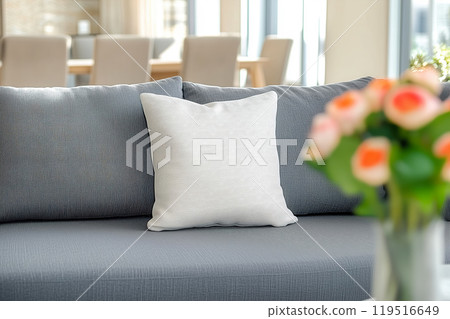 Cozy living room scene with a gray couch featuring a white pillow and a vase of fresh flowers in 119516649