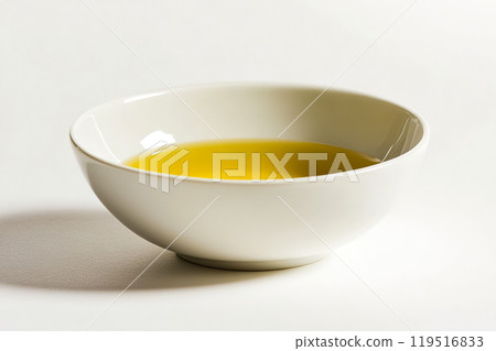 A close-up view of golden olive oil in a white bowl on a clean surface, showcasing its rich color A close-up view of golden olive oil in a white bowl on a clean surface, showcasing its rich color 119516833