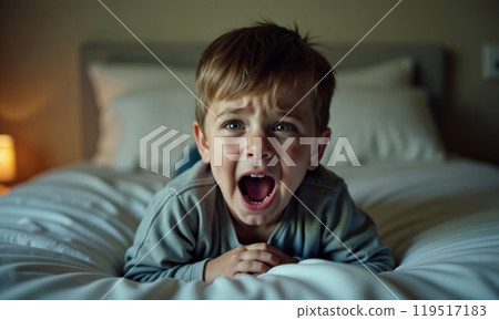 A boy lies on a bed, mouth open, making a funny face 119517183